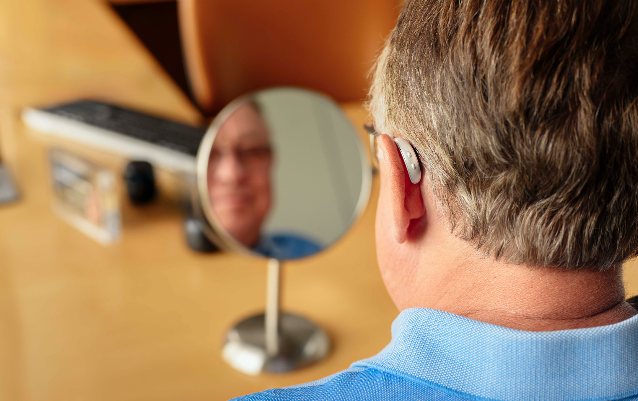 Man with hearing aid on ear looking in mirror